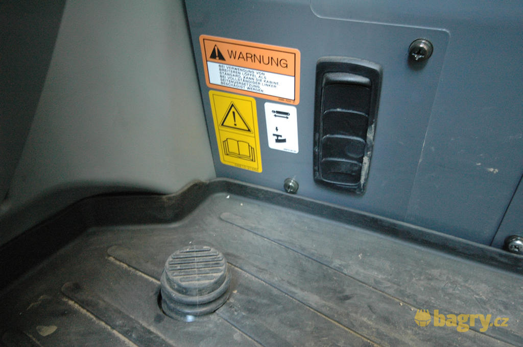 Tlačítko hydraulického rychloupínače, na které se musí stoupnout společně se stlačením tlačítka na joysticku